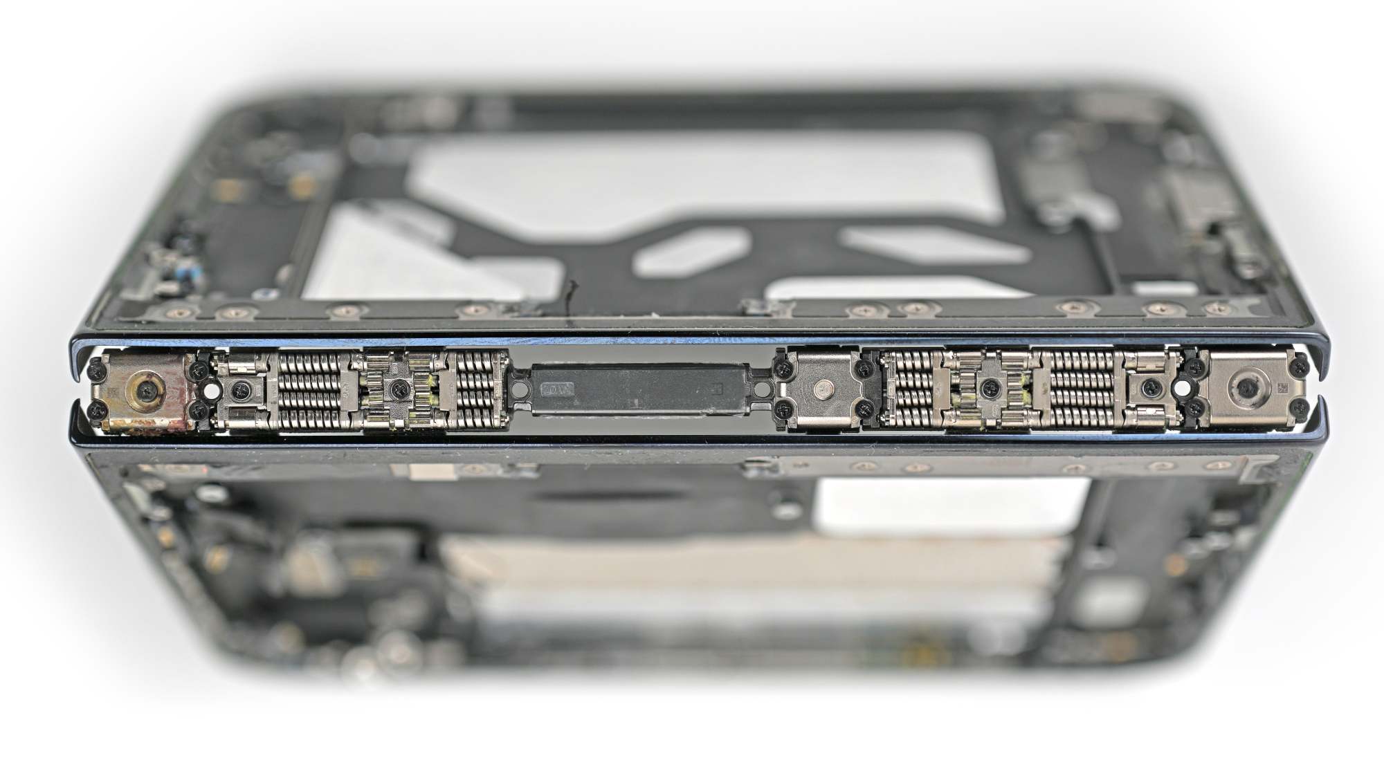 View along the spine of a stripped-down iPhone Duo folded shut, showing rows of small coiled springs and metal hinge mechanisms along the fold, with the frame behind out of focus.